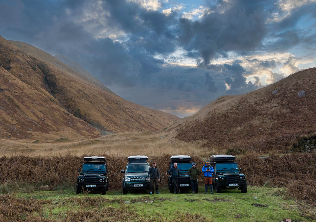 Four Land Rovers vehicles lined up in a mountainous Scottish landscape