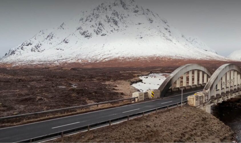 Opening scene of the Nomadic Scotland video, picturing a bridge at Glen Coe in winter, with snow on the mountains in the background.