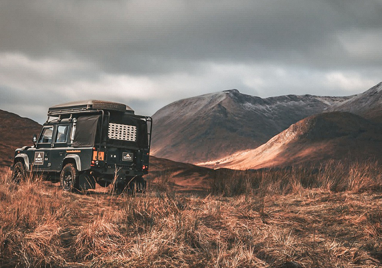 A Nomadic Scotland Land Rover parked on rugged Scottish moorland with mountains in the background