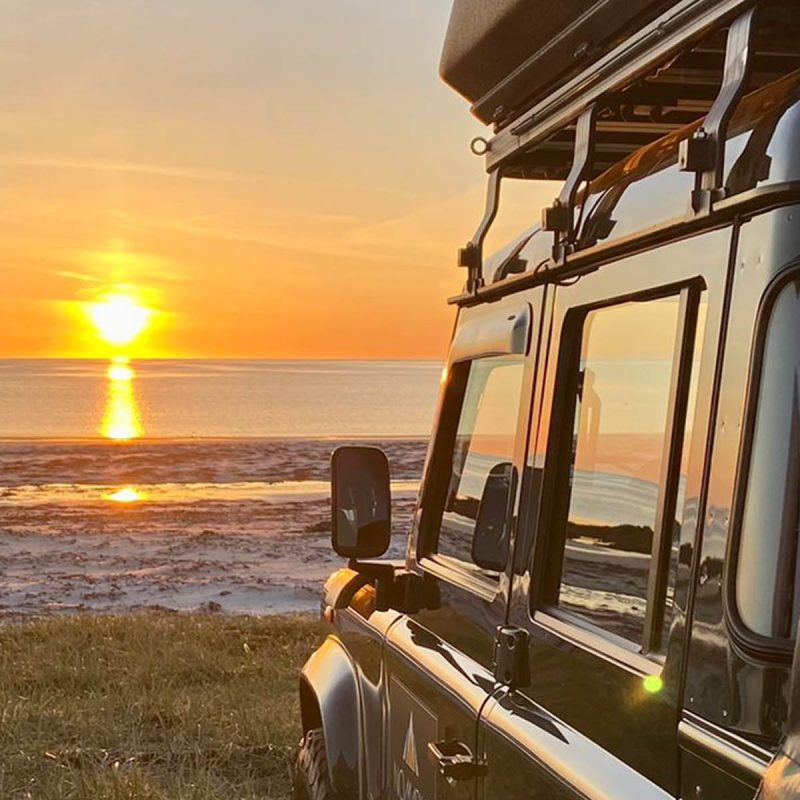 A Nomadic Scotland Land Rover overlooking a beach with a sunset in Scotland