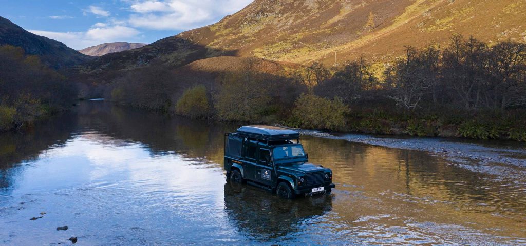 A Land Rover in water a t the foot of rolling hills