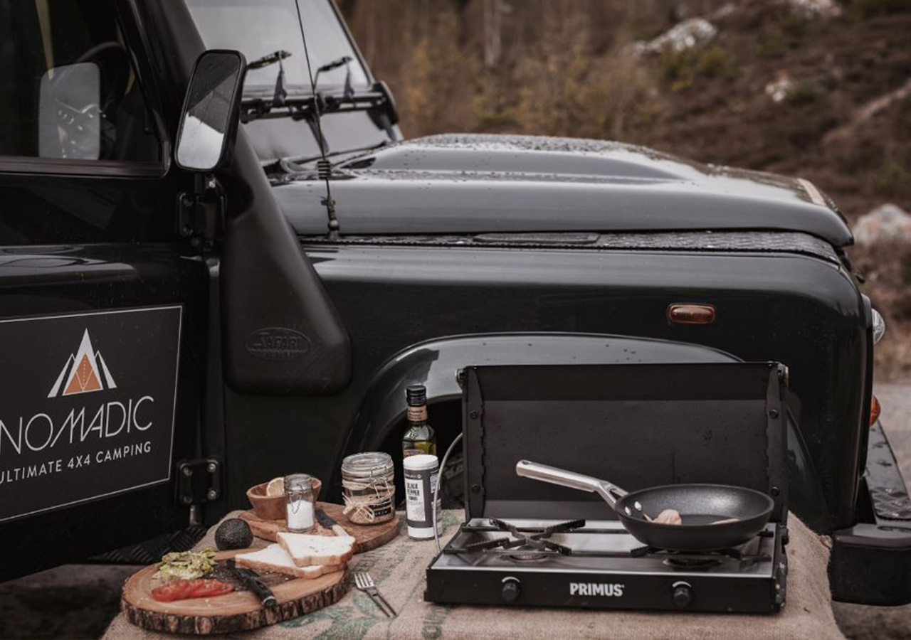 Camping cooking equipment set up next to a Nomadic Land Rover.