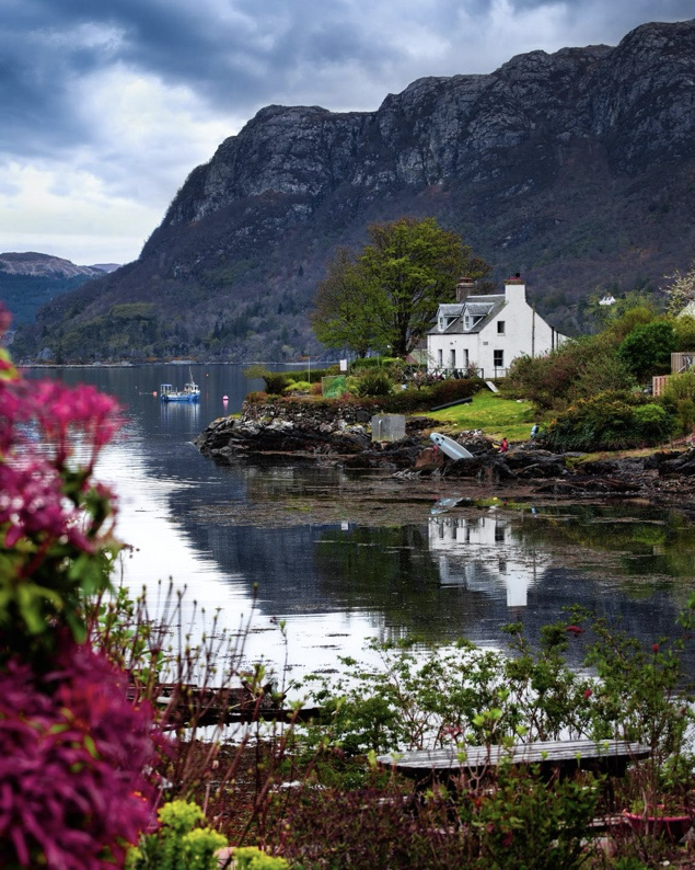 Beautiful calm waters by a white cottage with imposing mountains in the background in Plockton, Scotland