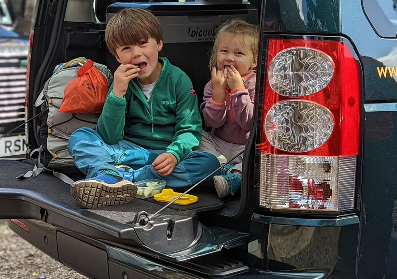 Two kids in the back of a 4x4 eating food on a Nomadic Scotland road experience