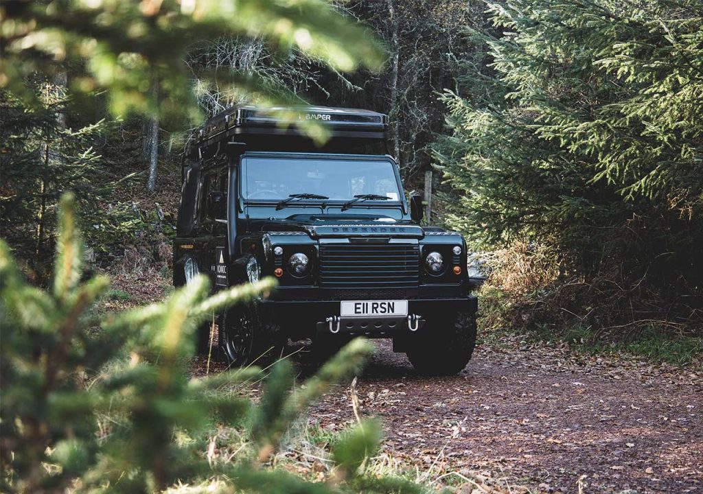 A Land Rover Defender driving through a woodland road