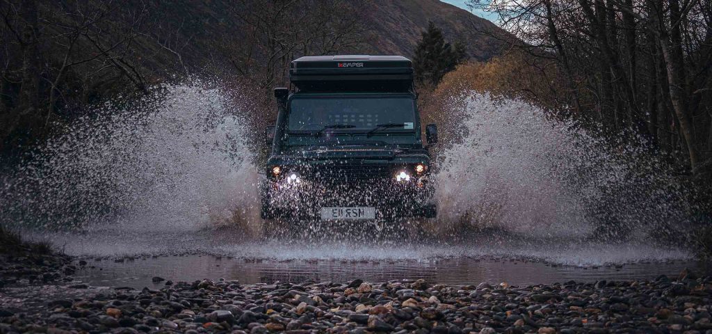 A Land Rover experience in the Scottish Highlands splashes through water in the winter.