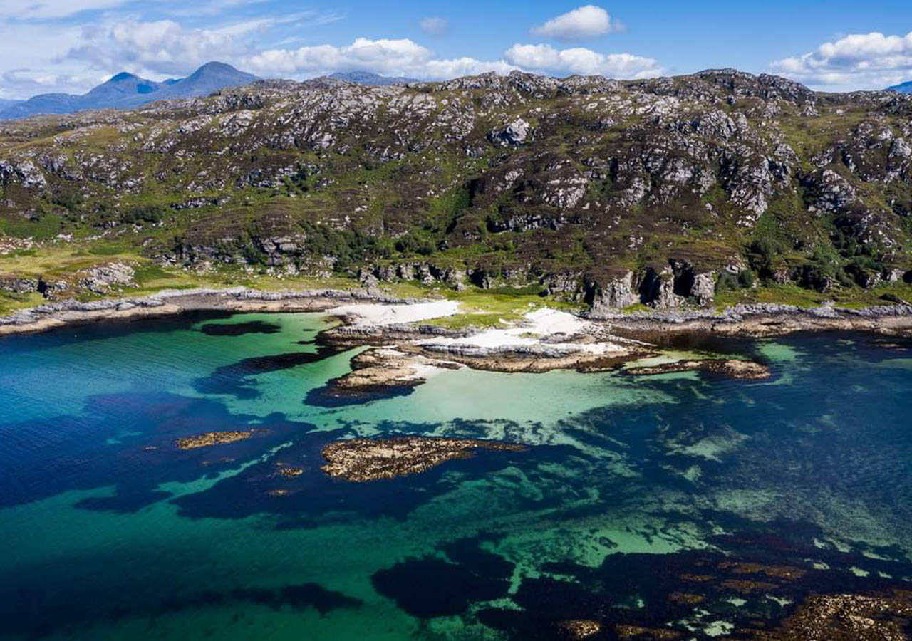 Stunning Scottish scenery - a rugged coastline, turquoise blue sea and mountains in the background