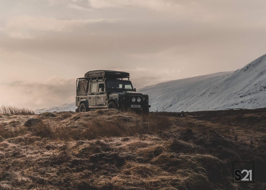 Car perched on hill overlooking Scottish mountains.