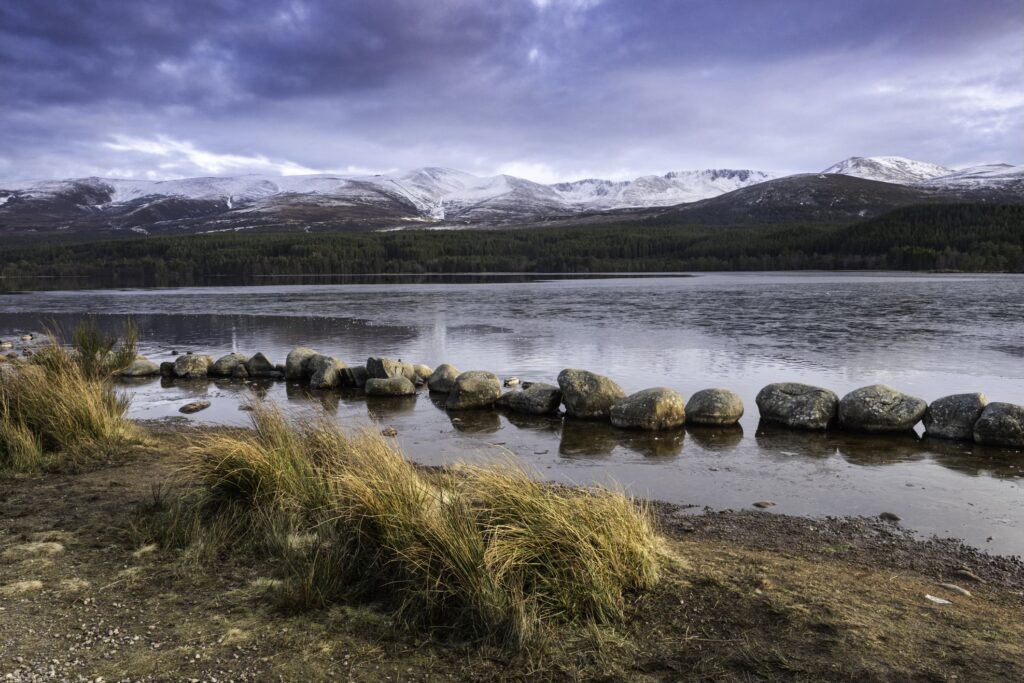 Loch Morlich in the Cairngorms, below snow covered mountains.