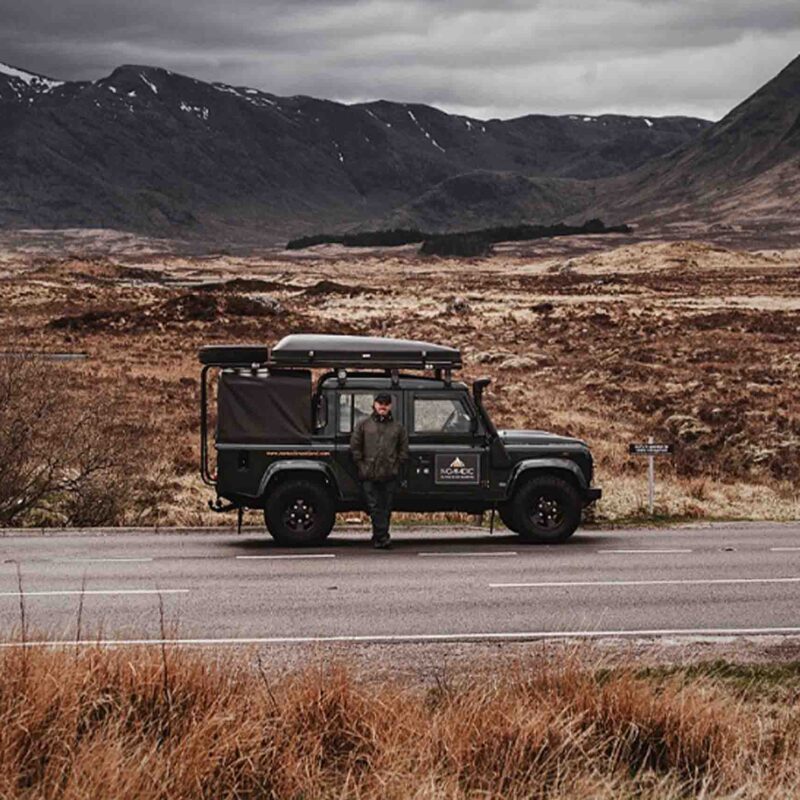 A 4x4 on a road with a happy driver standing next to it.