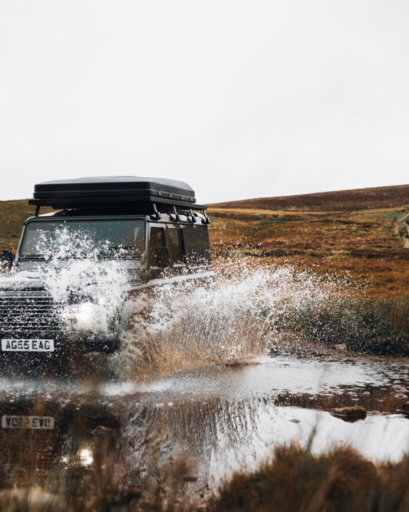 Nomadic Scotland Classic Defender 110 driving through water in Scottish Highlands