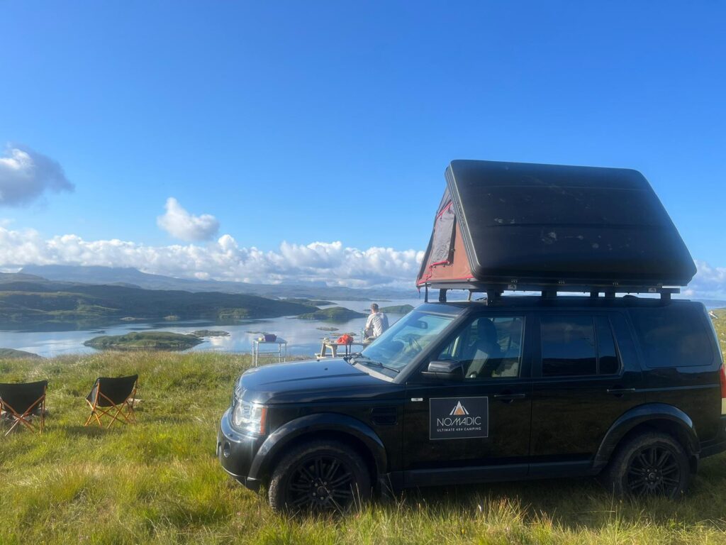 Nomadic Scotland Landrover pitched up on cliff, in summer, with beautiful view of Scottish Islands.